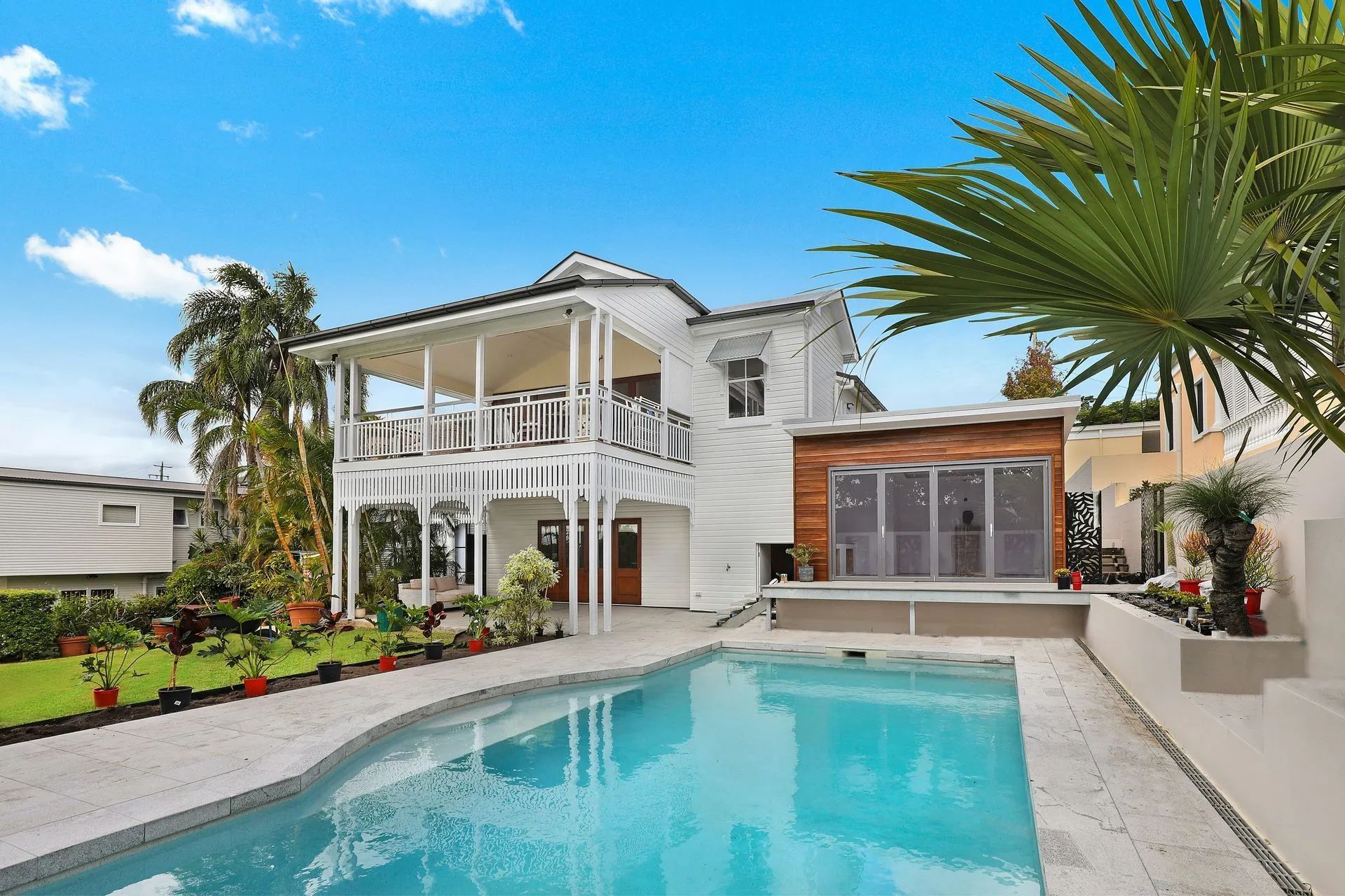 White house with a pool and balcony, set against a blue sky.
