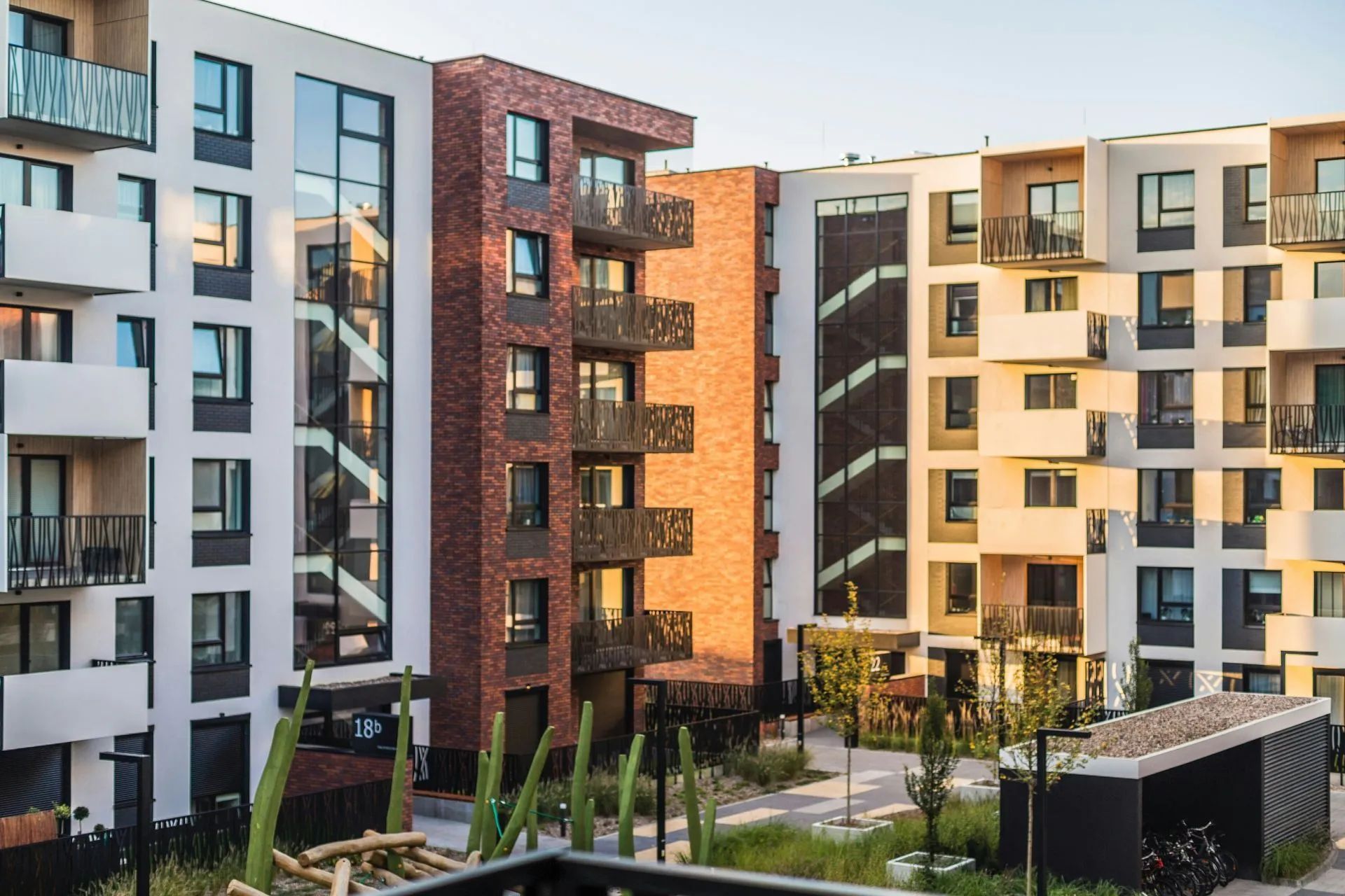 Modern apartment complex with brick and white facades; balcony views; sunny outdoor setting.