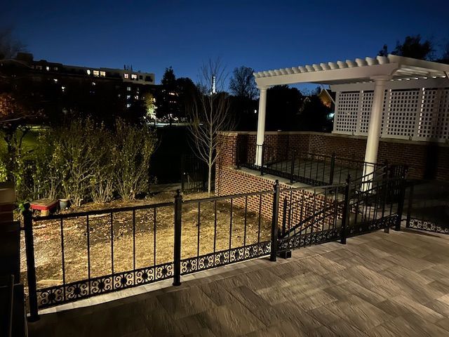 Nighttime backyard patio with pergola, black fence, and landscaped garden beds.