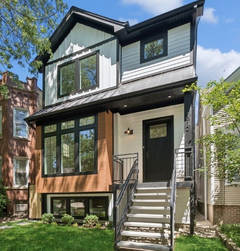 Two-story modern house with black trim, front steps, and a small landscaped yard.
