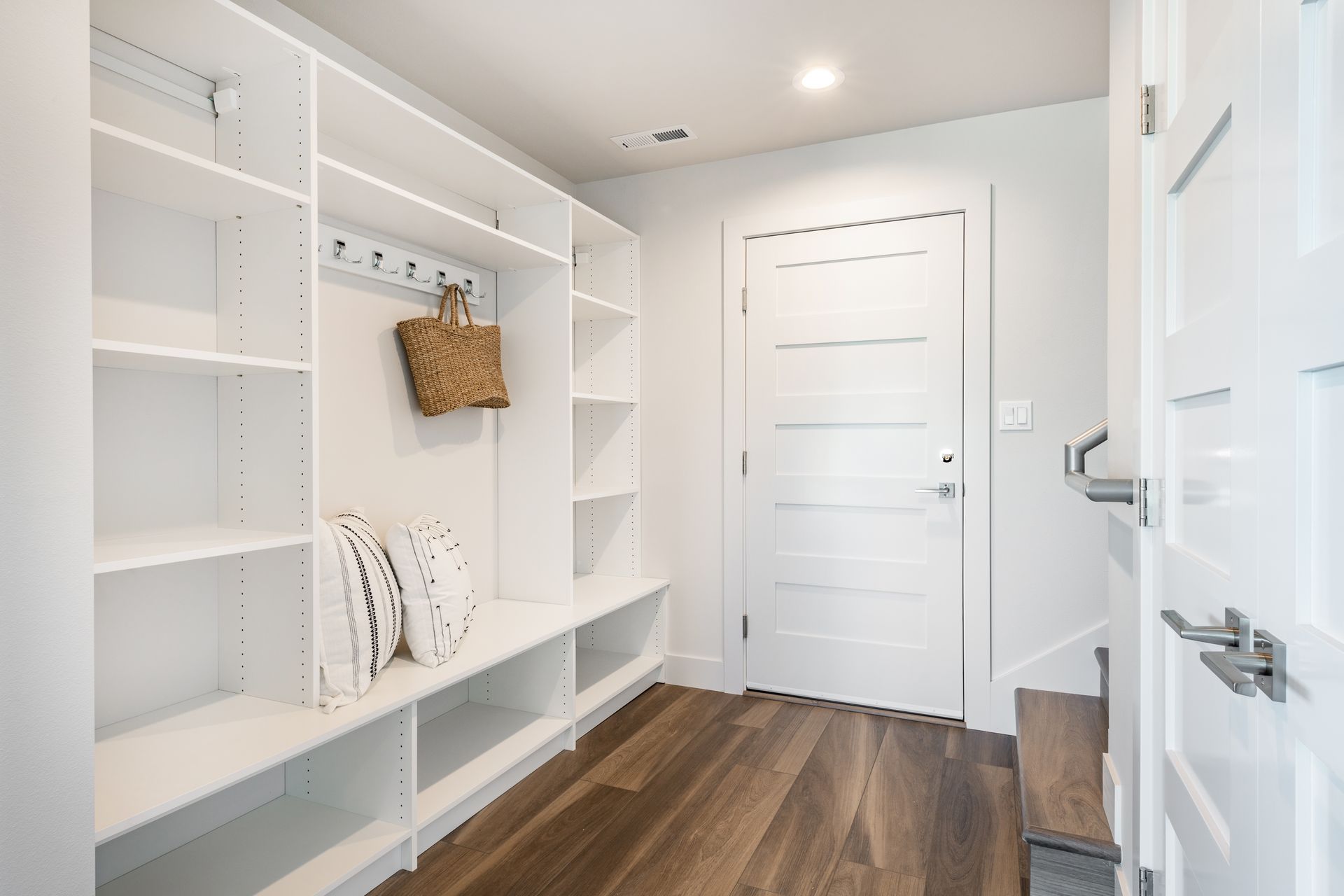Bright built-in mudroom shelves with baskets and hooks beside a white door and dark wood floor.
