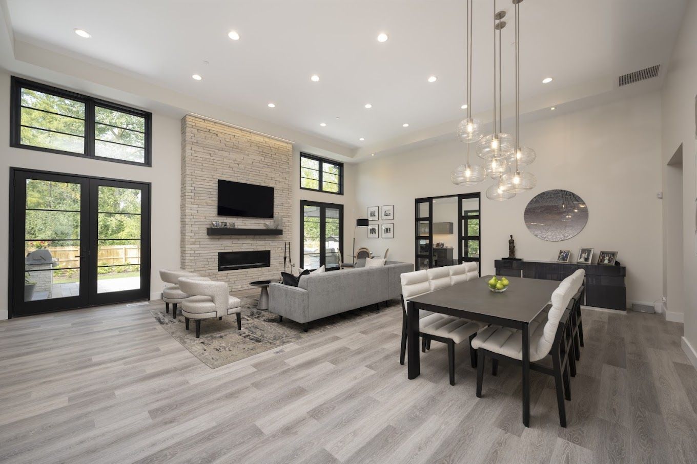 Modern open-concept living room and dining area with gray furniture, black-framed windows, and a mounted TV.