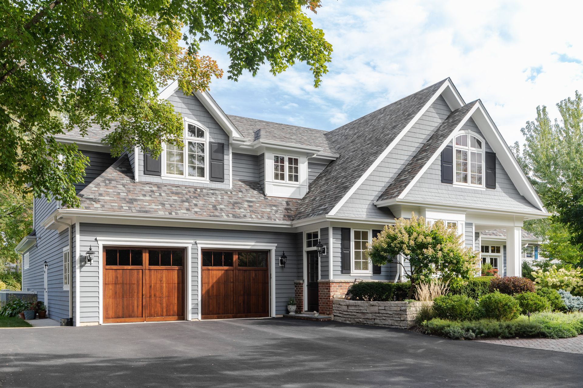 Gray suburban house with two wooden garage doors, gabled roof, and landscaped front yard