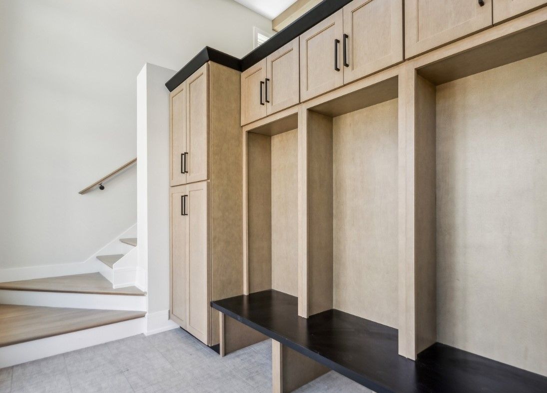 Built-in hallway storage bench with light wood cabinets and black seat beside a staircase