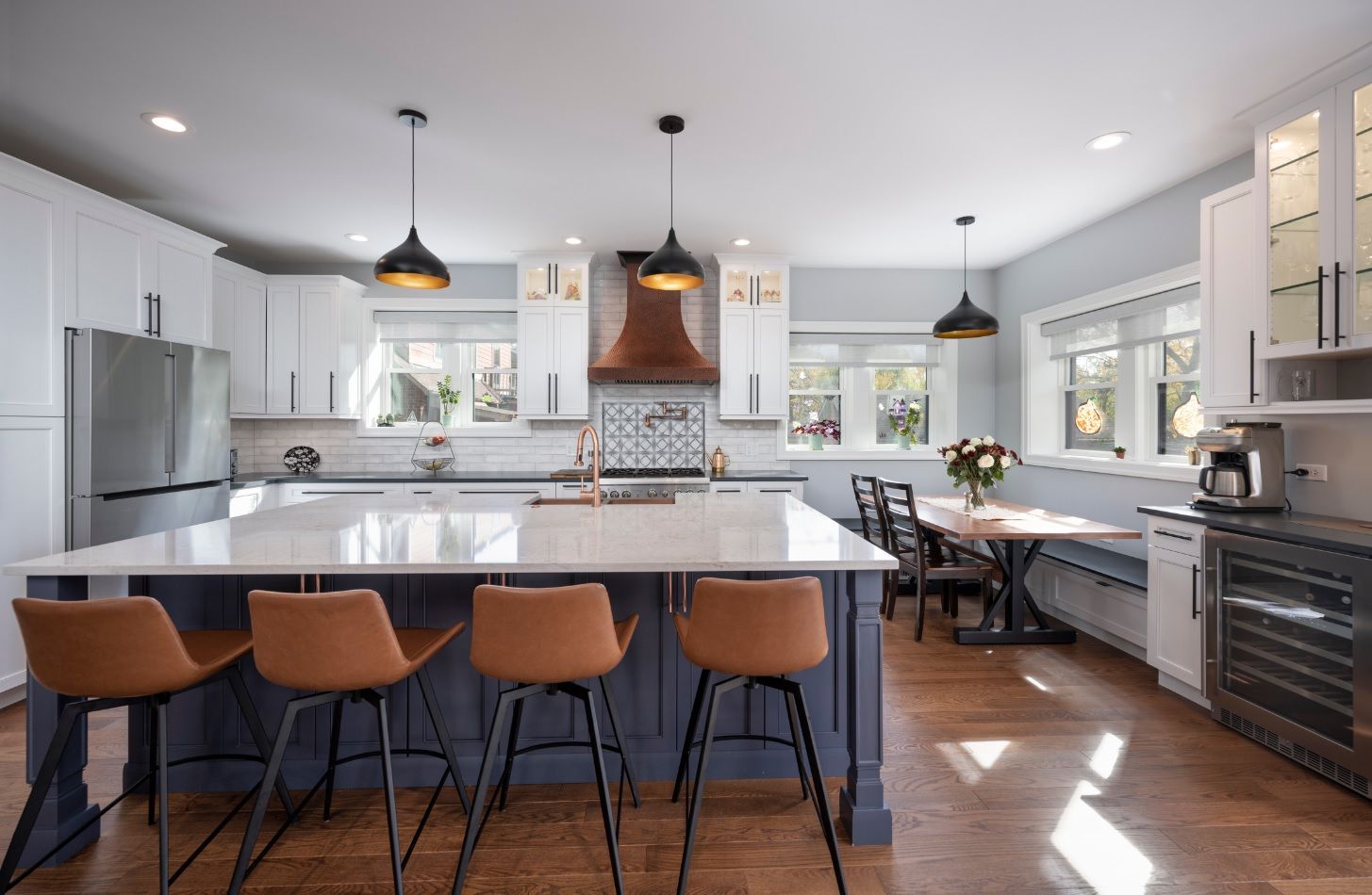 A kitchen with a large island , stools , a table and a refrigerator.