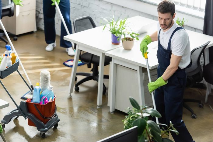 A man is cleaning the floor of an office with a mop