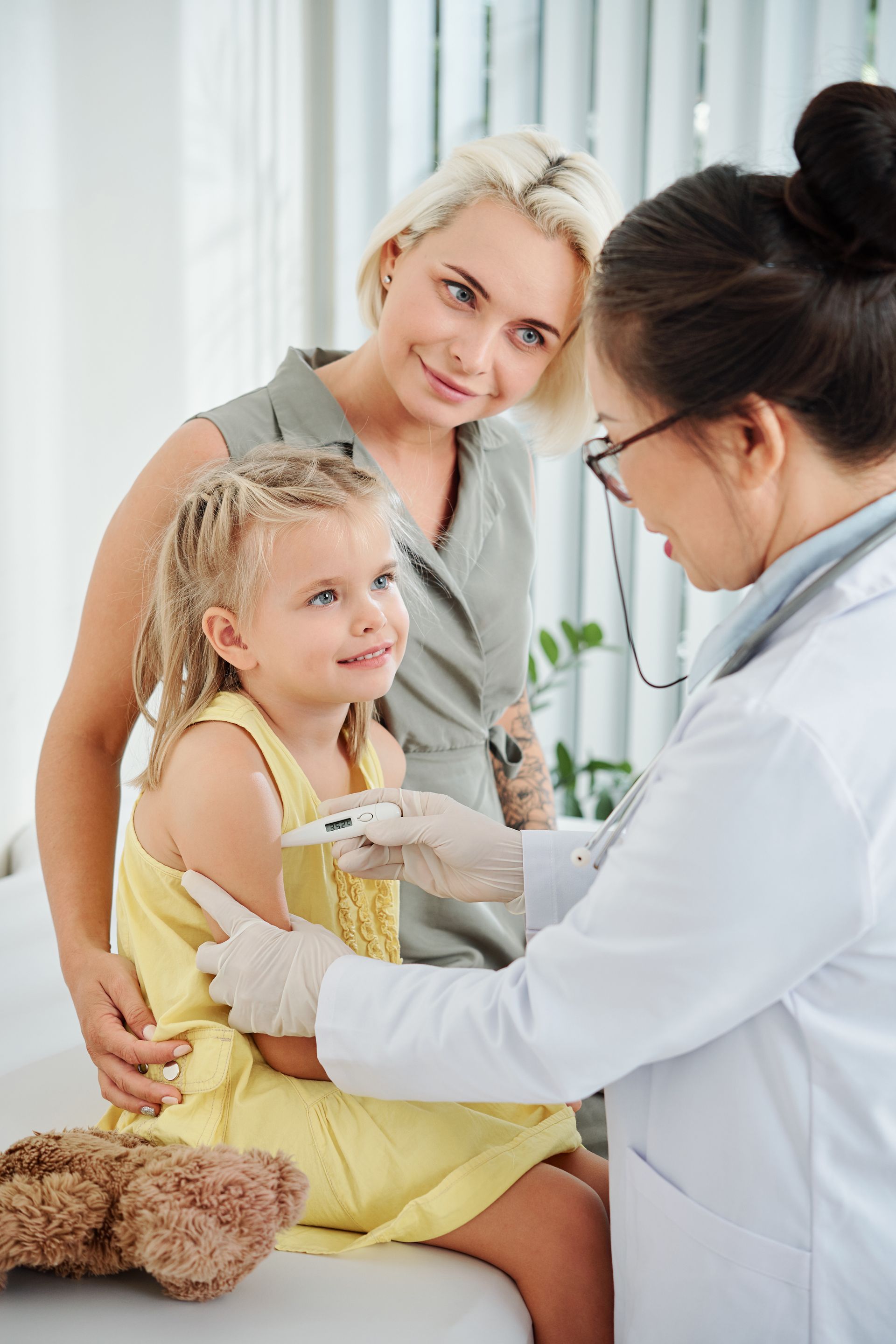 A little girl is sitting on a couch while a doctor examines her ear.