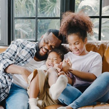 A man , woman and child are sitting on a couch laughing.