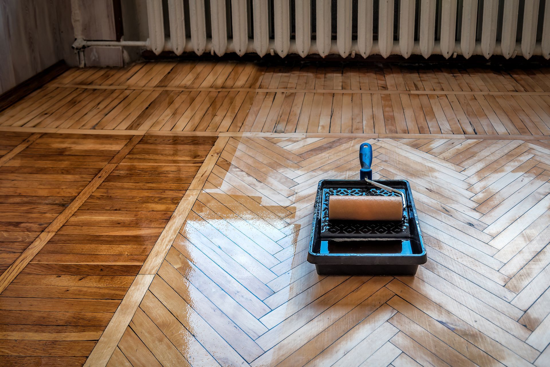 A wooden floor is being painted with a roller and tray.