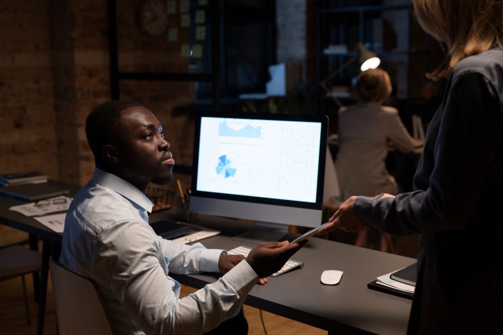 Two people discussing a presentation at a desktop computer in a dim office