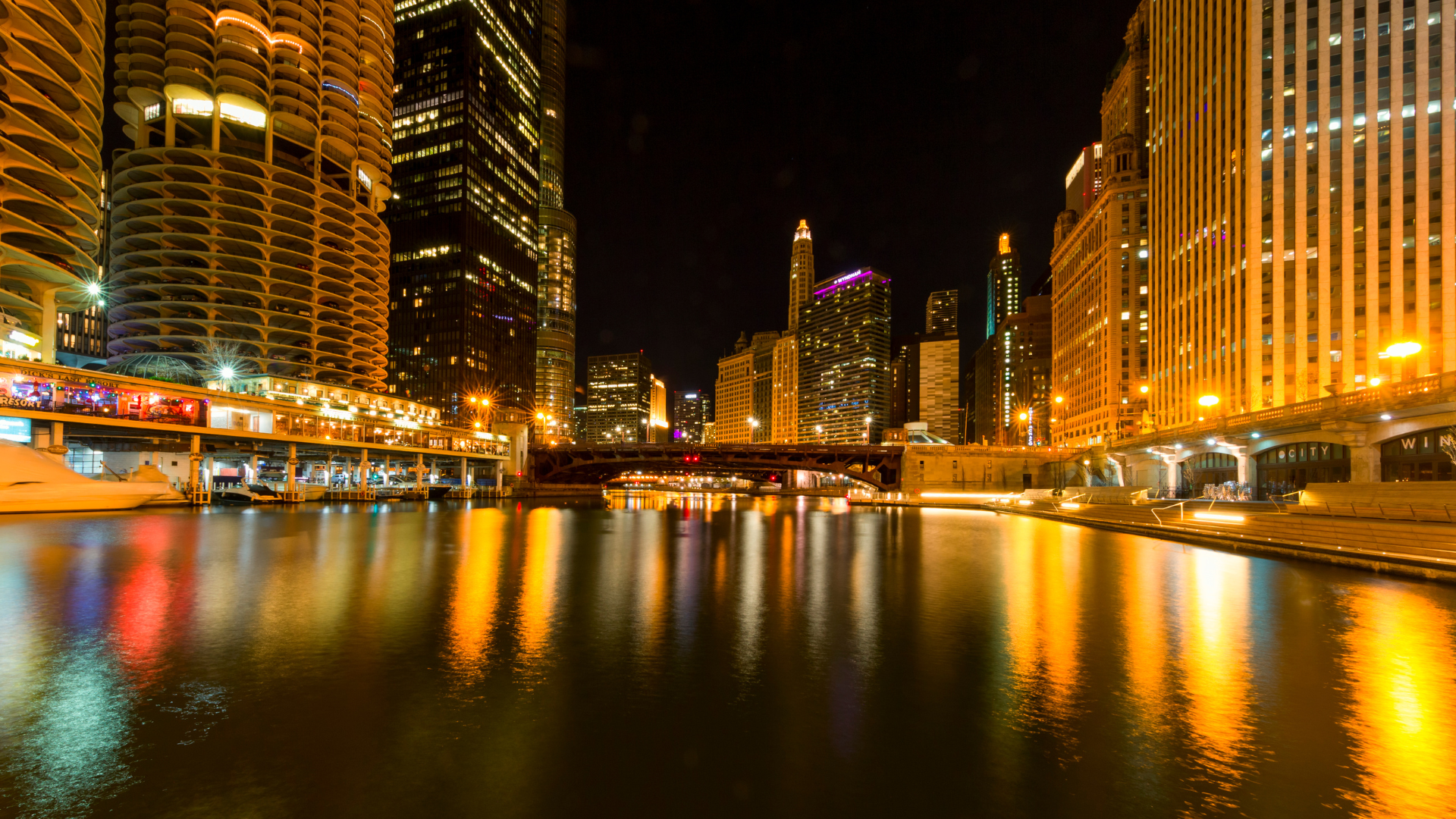 Nighttime city skyline with illuminated skyscrapers reflected in a calm river.