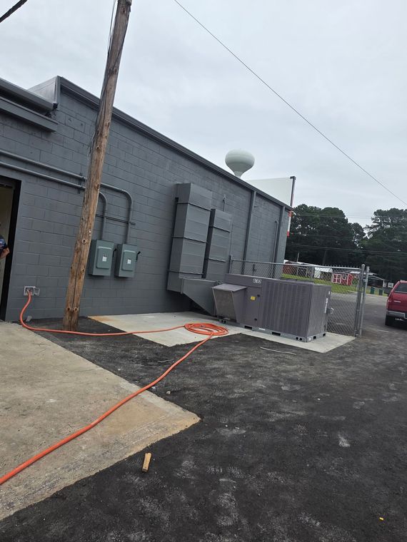 Gray utility building exterior with electrical panels, stacked pavers, and orange extension cord on gravel lot