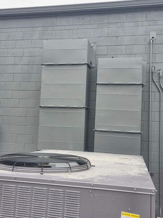 Outdoor HVAC units against a gray brick wall, with a white cooling unit in the foreground.