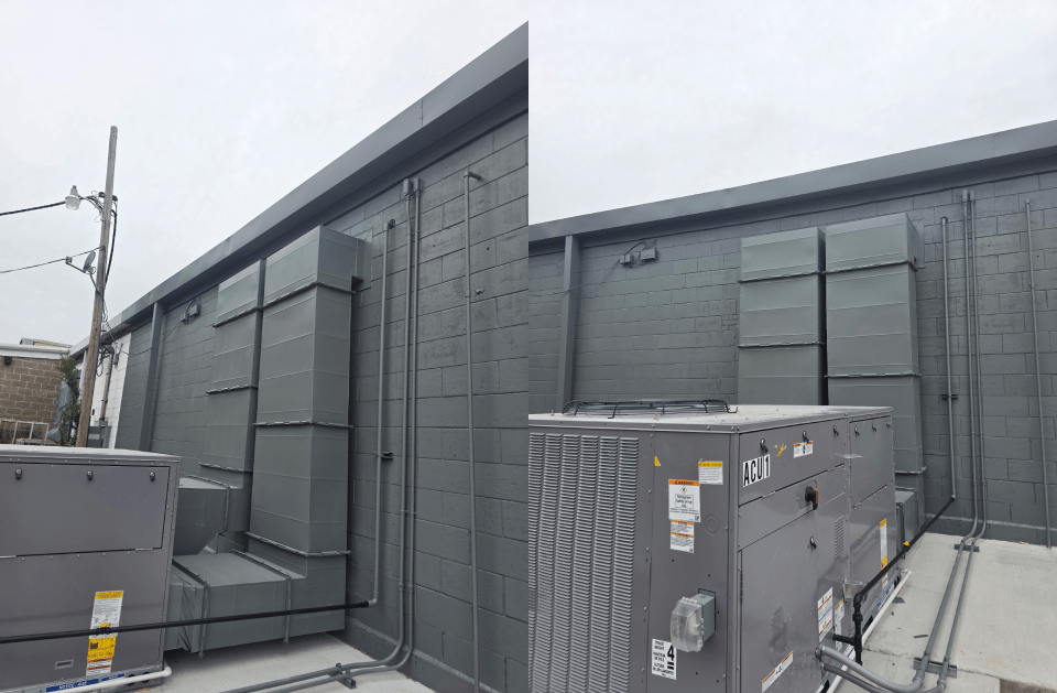 Rooftop HVAC units and ductwork beside a gray industrial building under an overcast sky