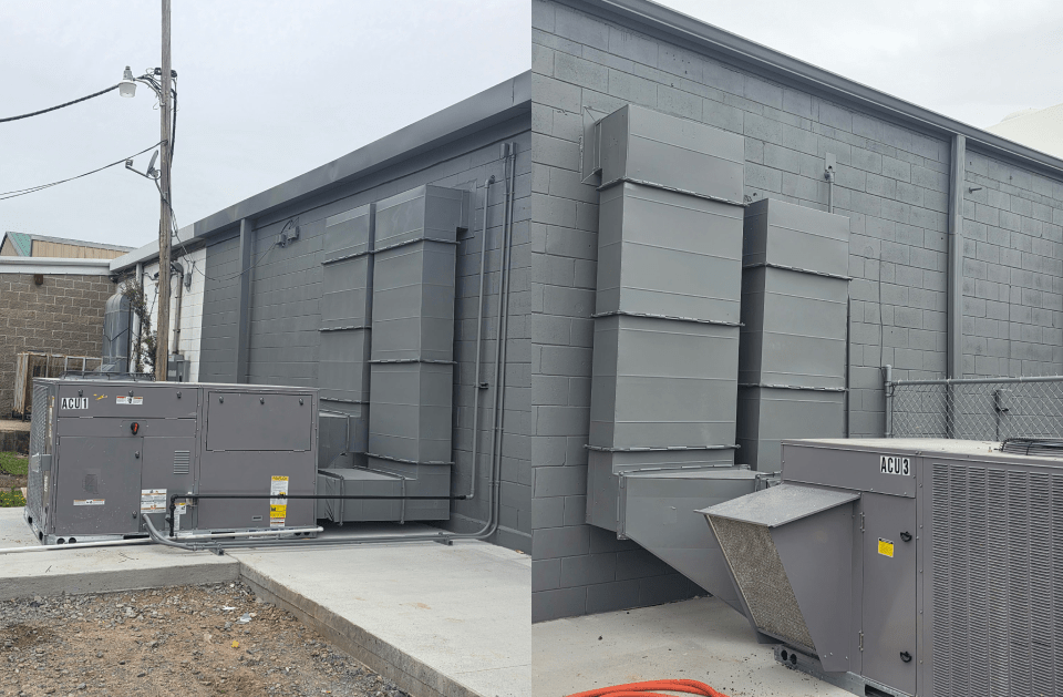 Gray industrial building exterior with large metal vents and utility boxes on a gravel lot