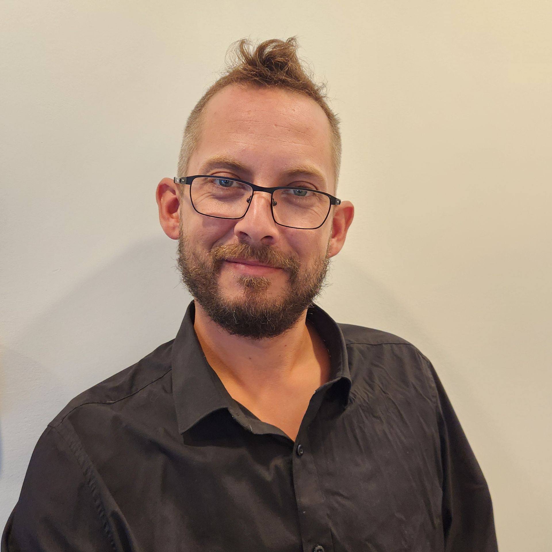 Un homme avec une barbe portant des lunettes et une chemise noire