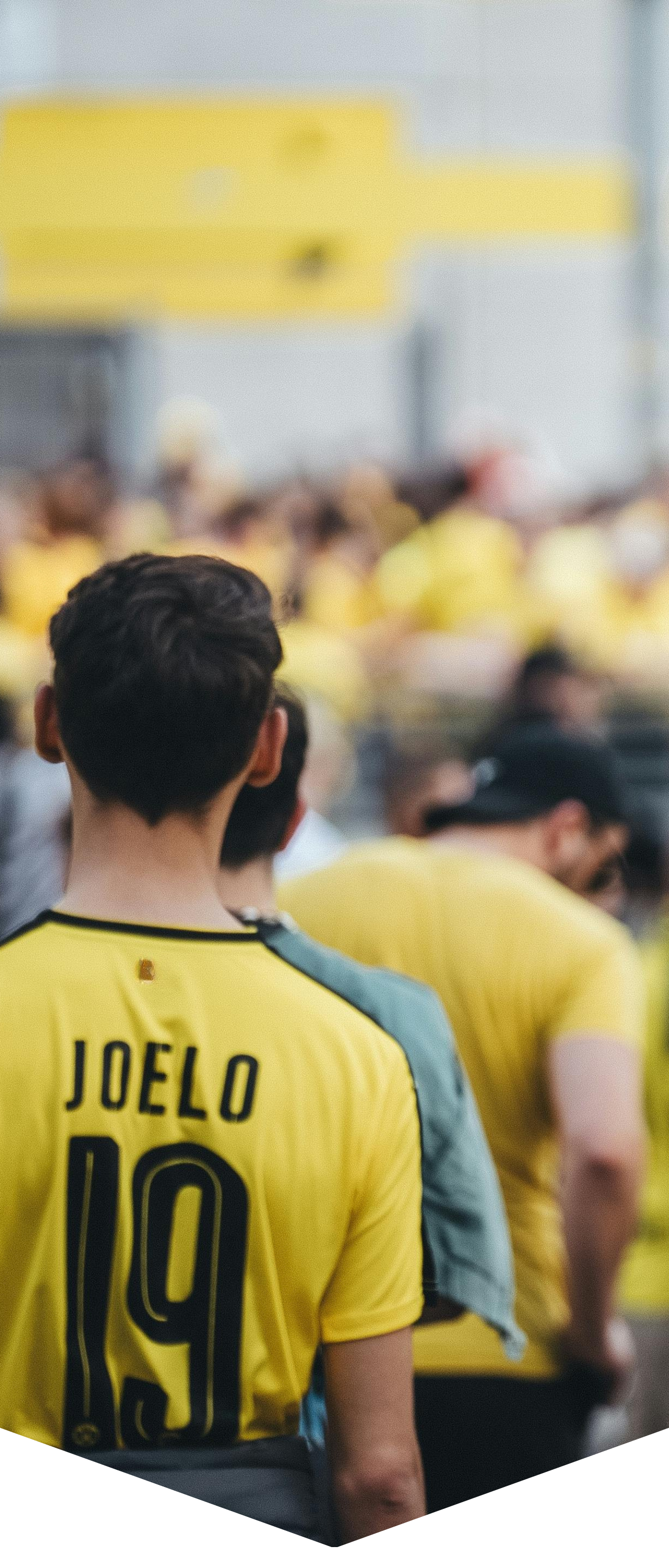 Publiek bij een voetbalwedstrijd, met een fan in een geel shirt met 