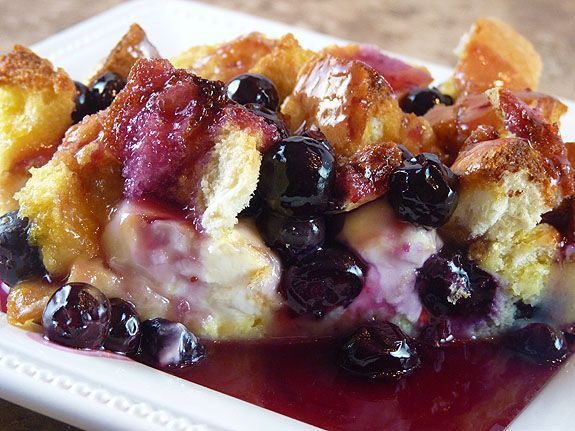 Bread pudding with blueberries and sauce on a white plate.
