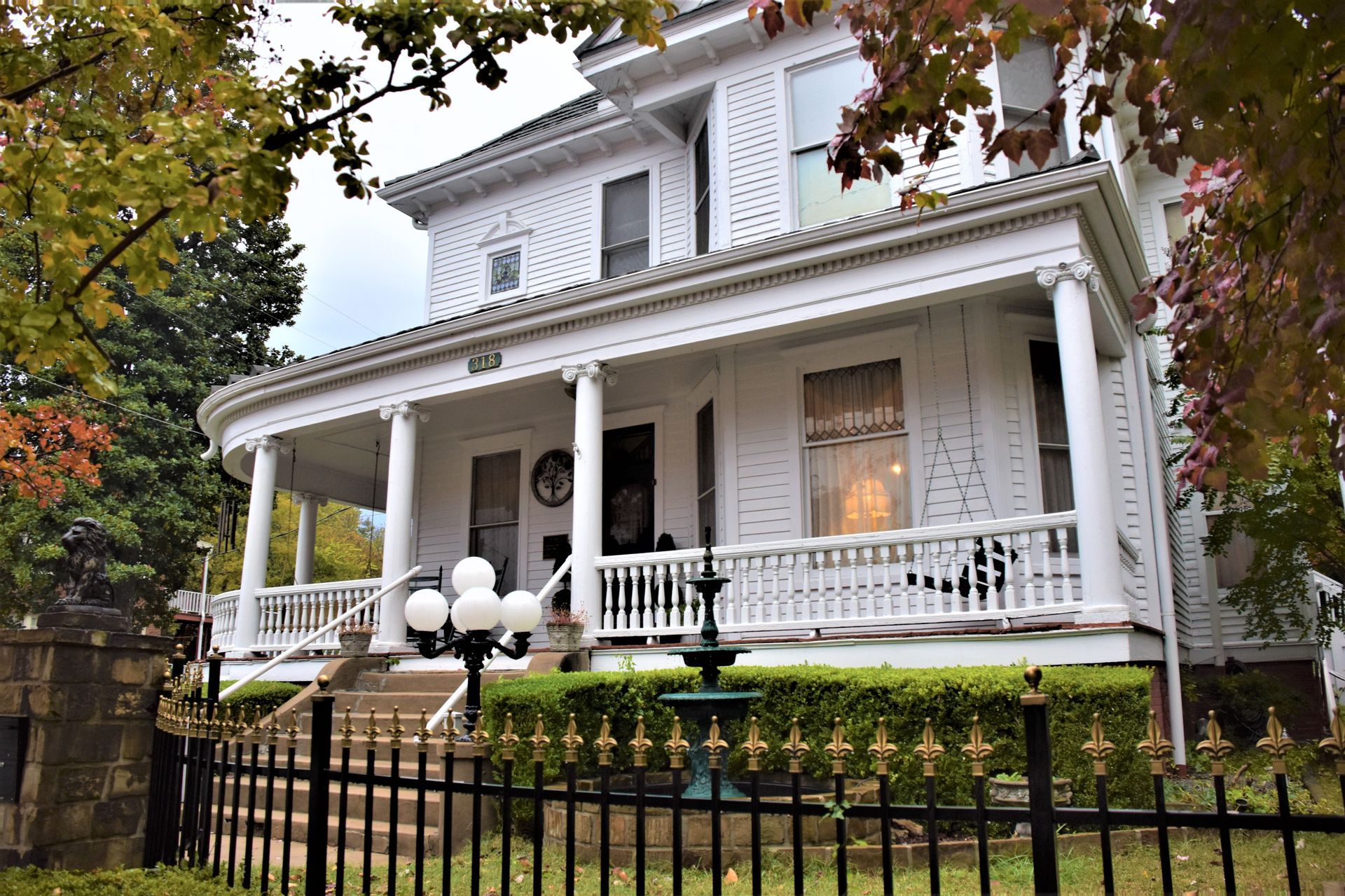 White Victorian house with wraparound porch, black fence, and lush greenery.