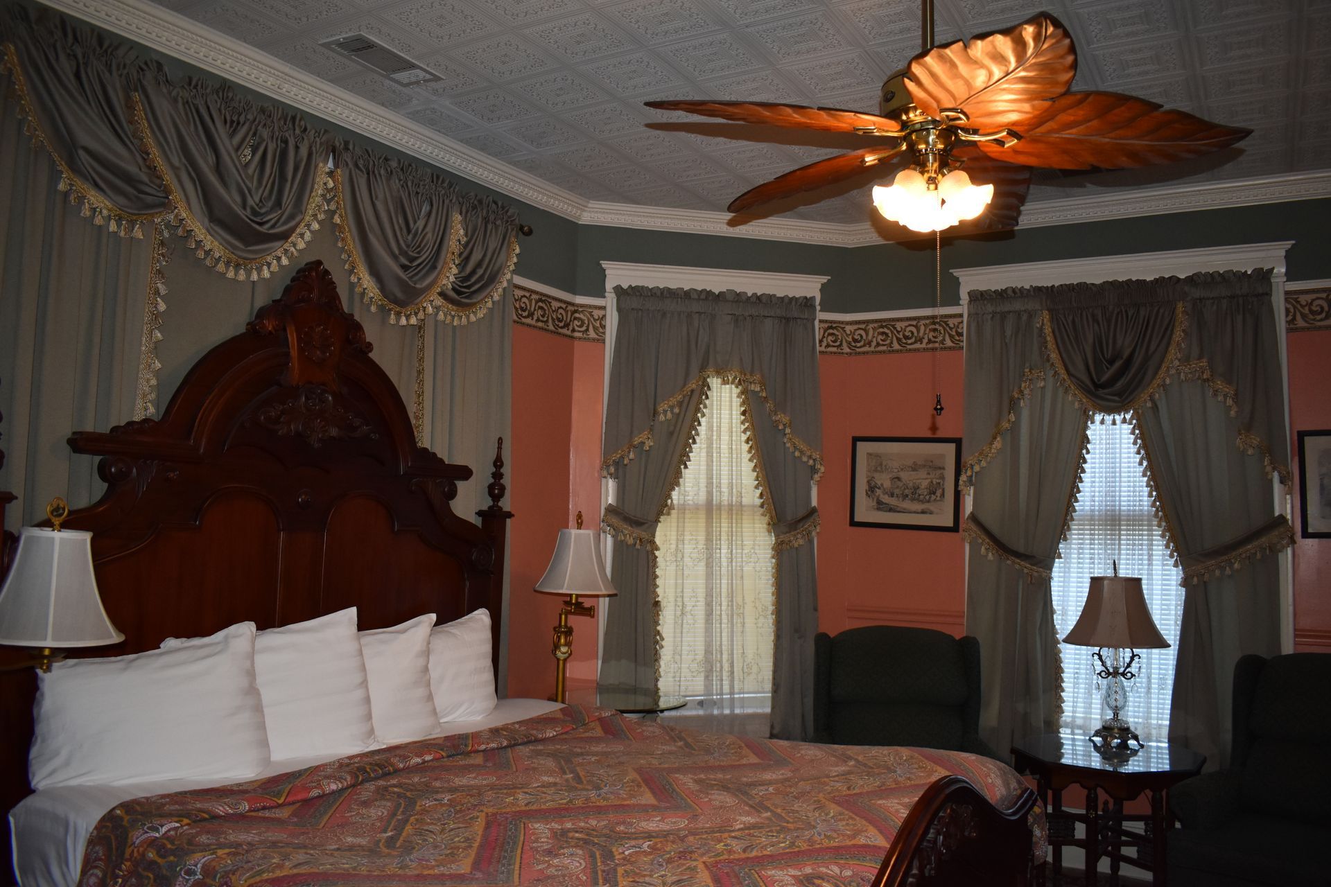 Bedroom with large wooden bed, ornate curtains, and a ceiling fan.