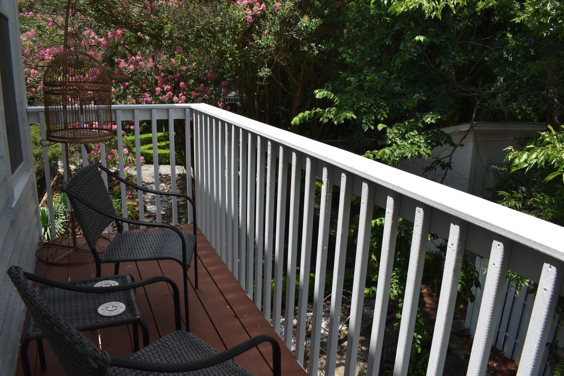 Balcony with two chairs, a birdcage, and lush greenery in the background.