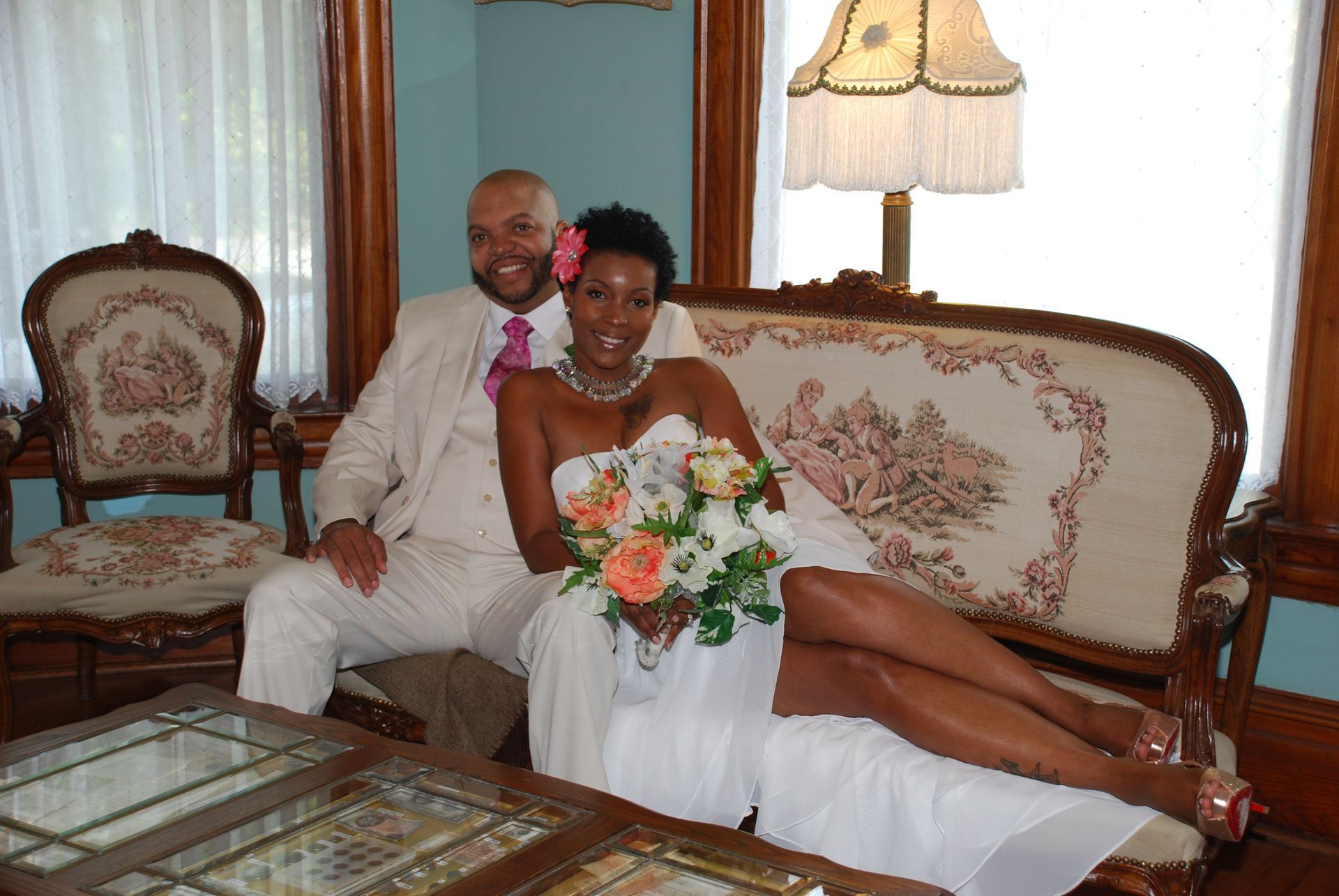 Newlywed couple posing on an antique couch; bride in white dress, groom in white suit.
