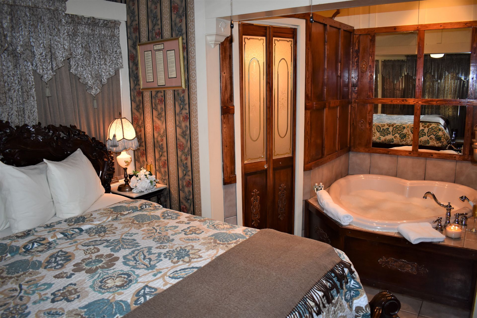 Bedroom with jacuzzi; bed has patterned comforter, carved headboard; wooden door, window to tub.