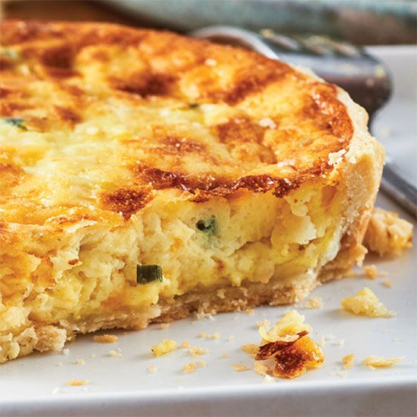 Close-up of a slice of quiche with a golden crust on a white plate.
