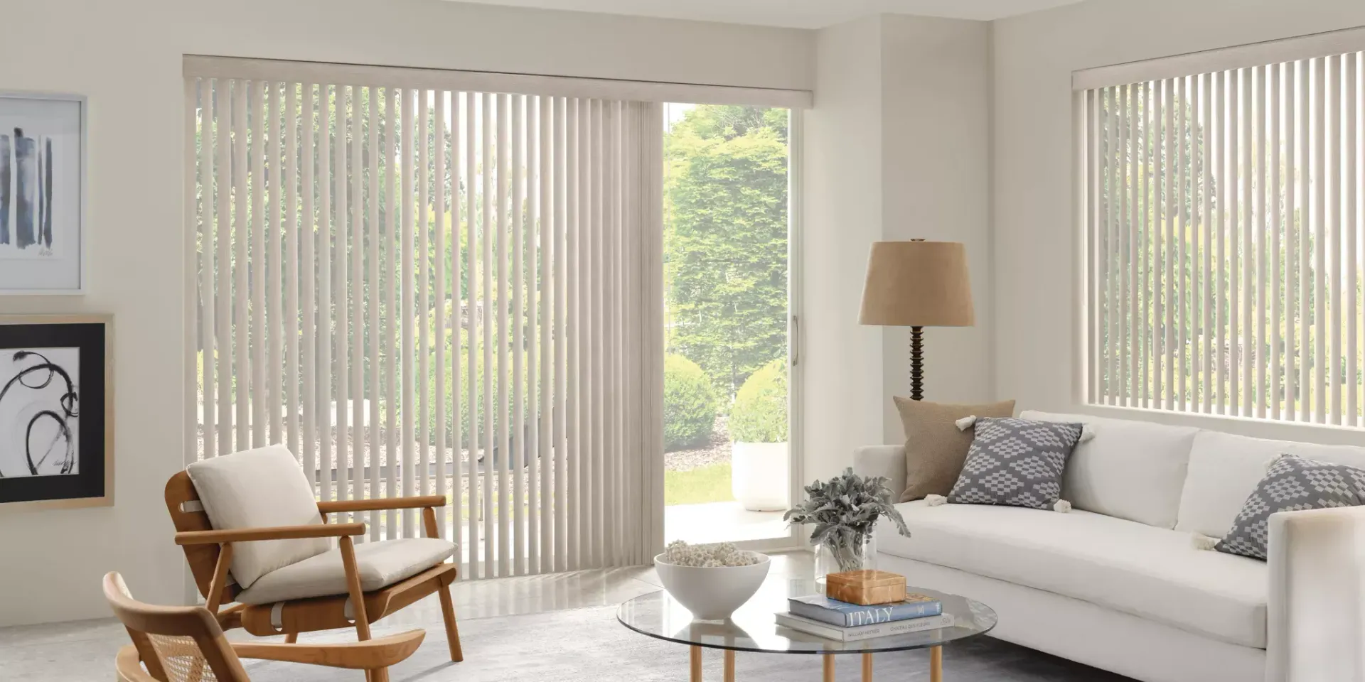 Living room with white vertical blinds, white couch, wooden chairs, and a glass coffee table.