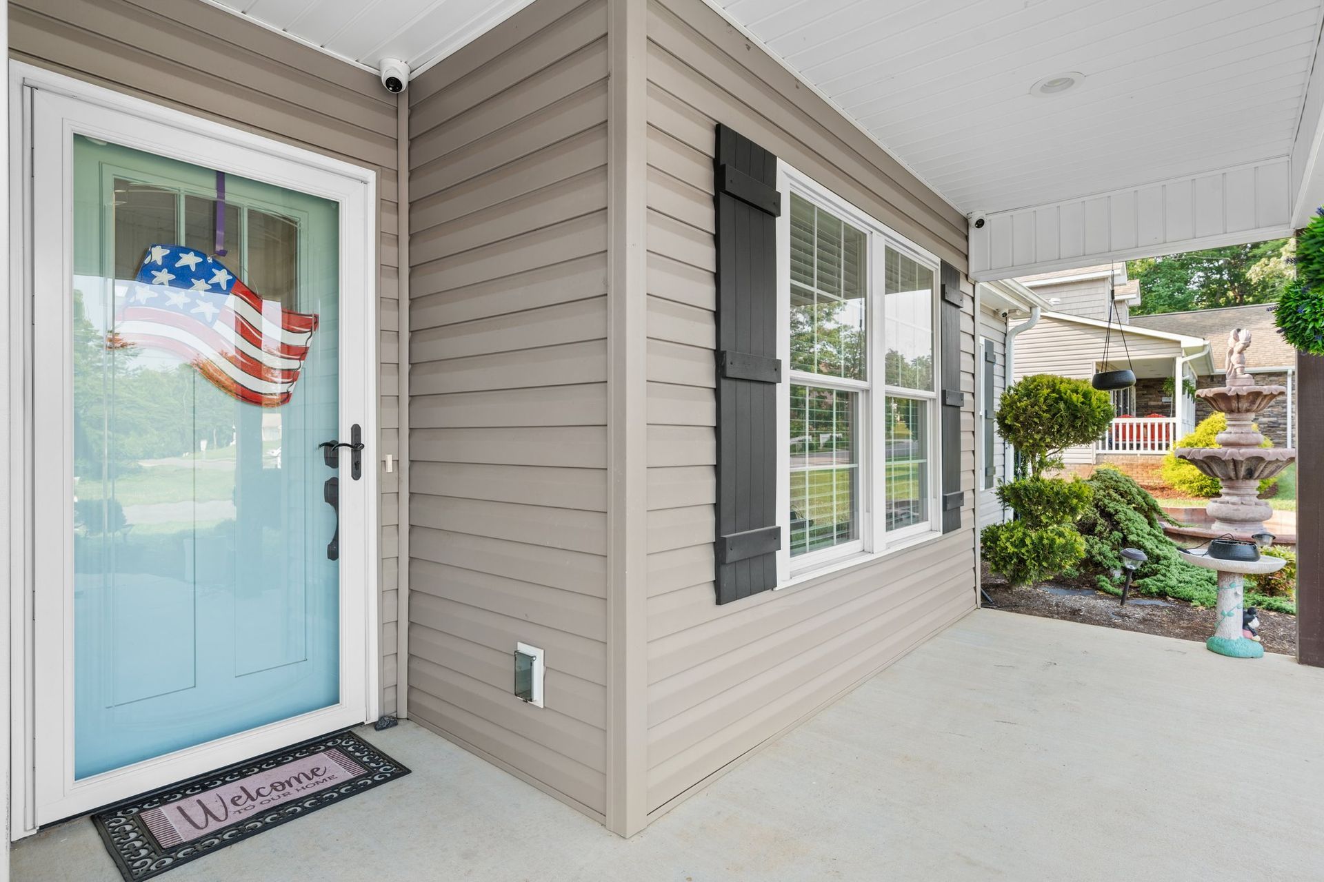 Front porch with a blue door, white railing, and beige siding beside a landscaped entryway