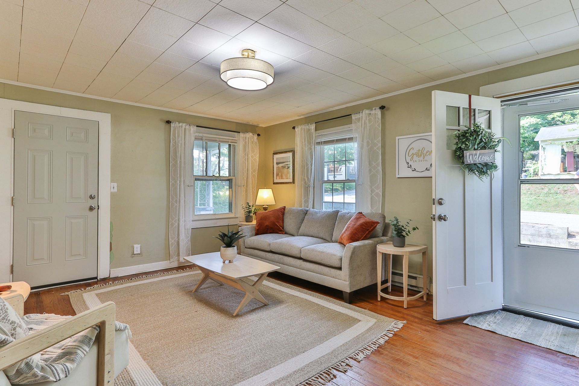 Bright living room with a sofa, rug, lamp, and open front door to a porch.