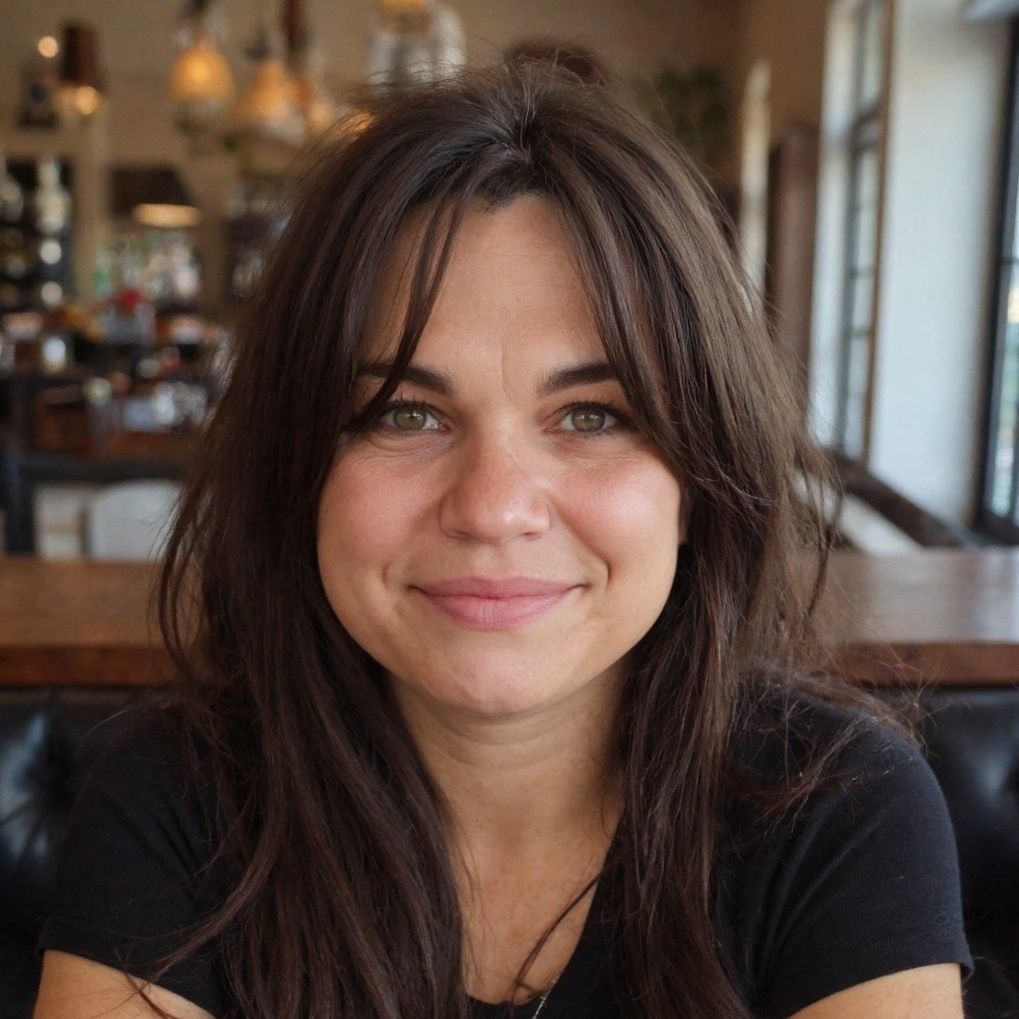 Smiling woman with dark hair seated in a warmly lit cafe