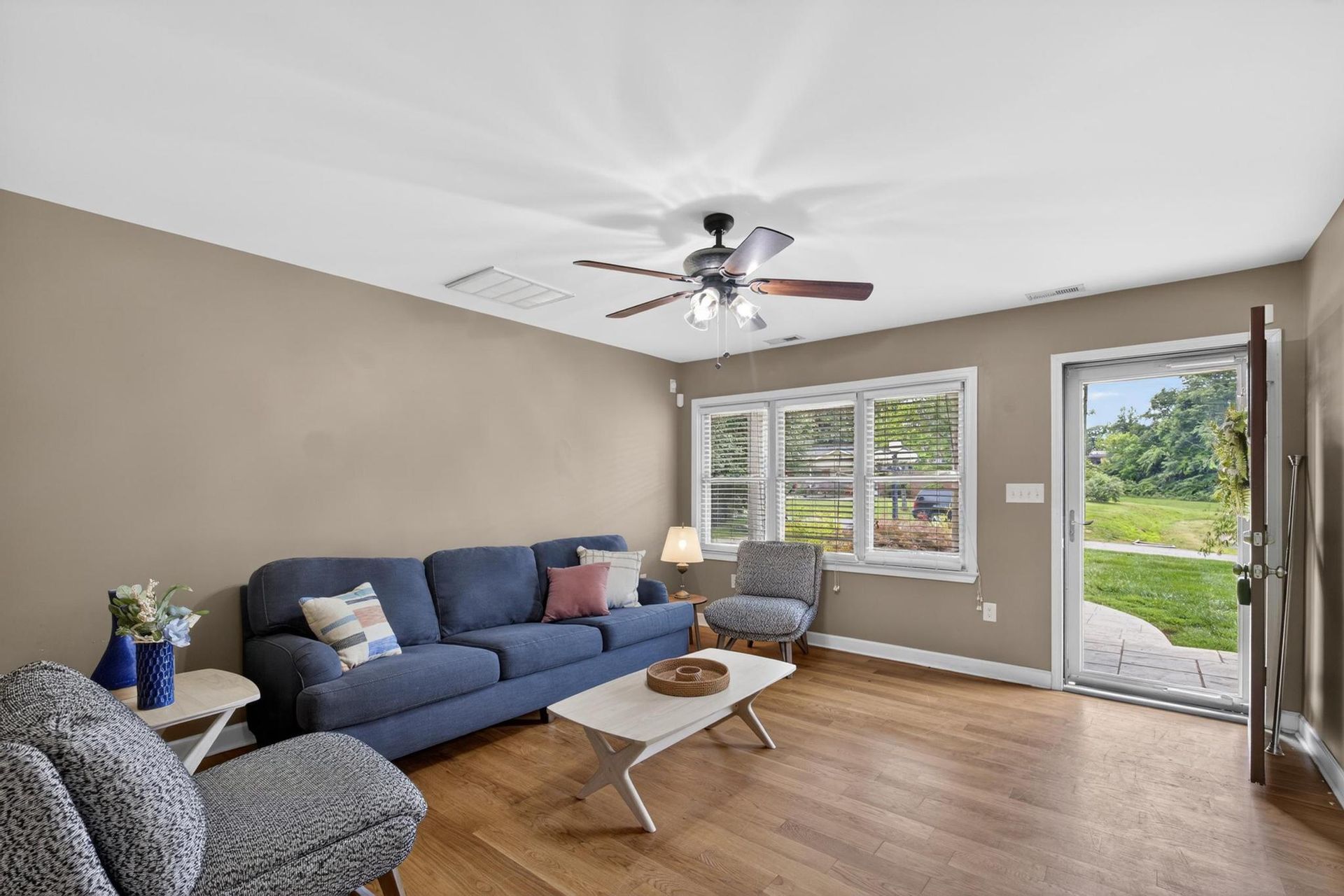 Bright living room with blue sofa, ceiling fan, and large windows overlooking a green yard