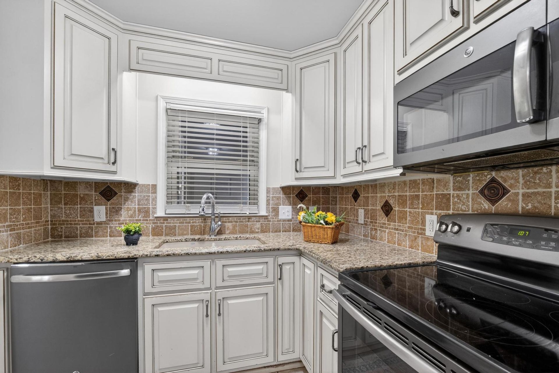 Bright white kitchen with stainless steel appliances, black stove, tan tile backsplash, and window over sink