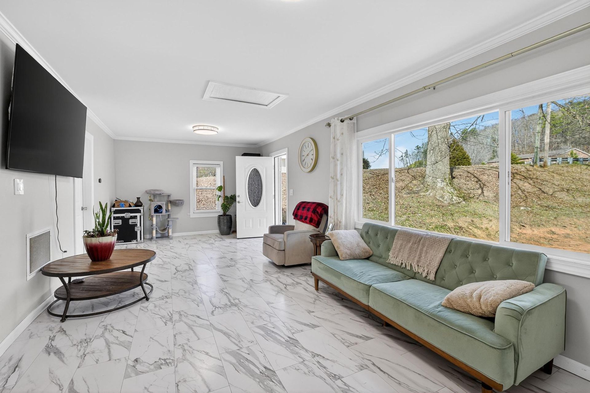 Bright living room with mint sofa, marble floor, wall-mounted TV, and large windows overlooking greenery
