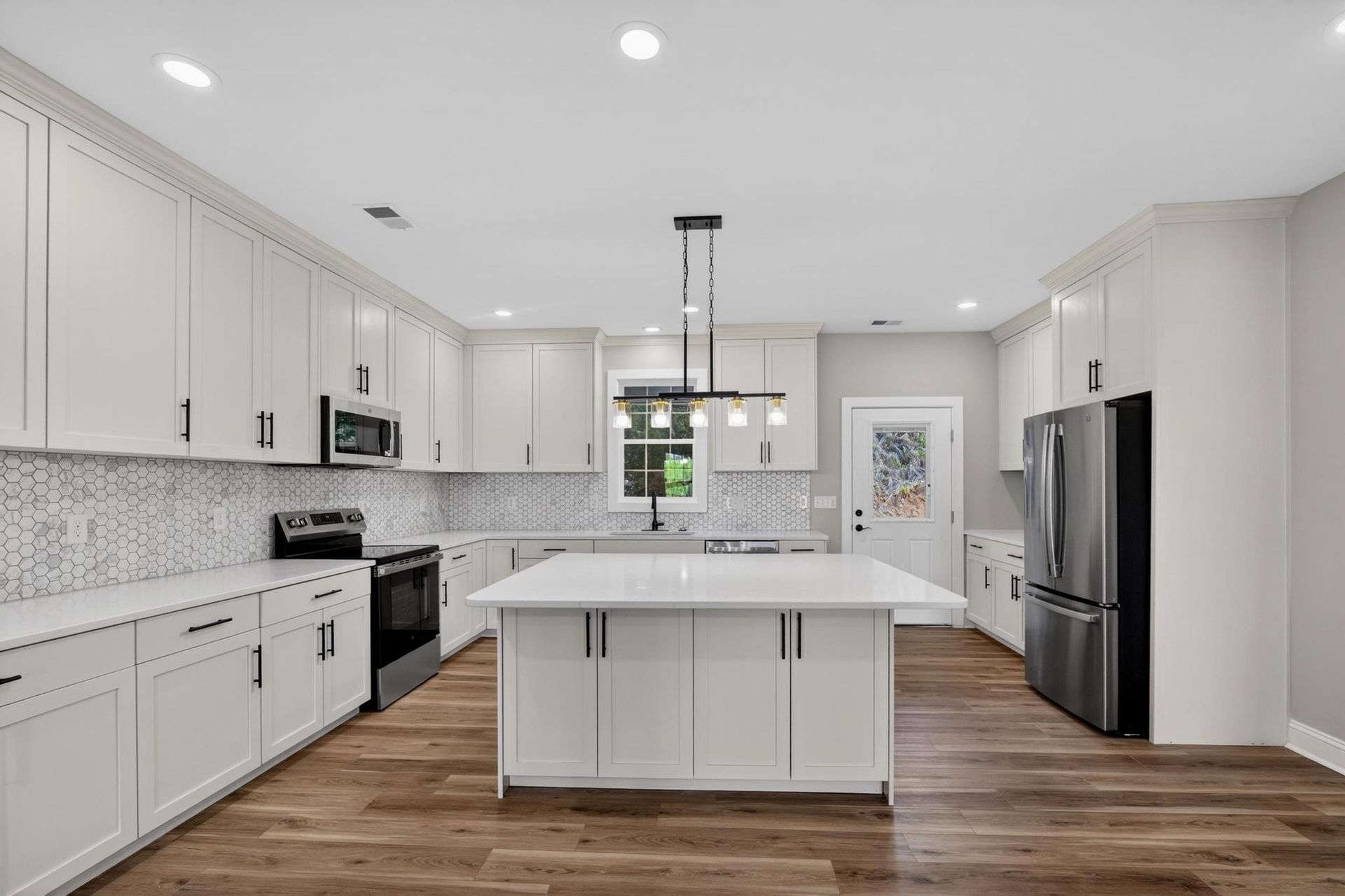 Bright modern kitchen with white cabinets, island, stainless steel appliances, and wood floors