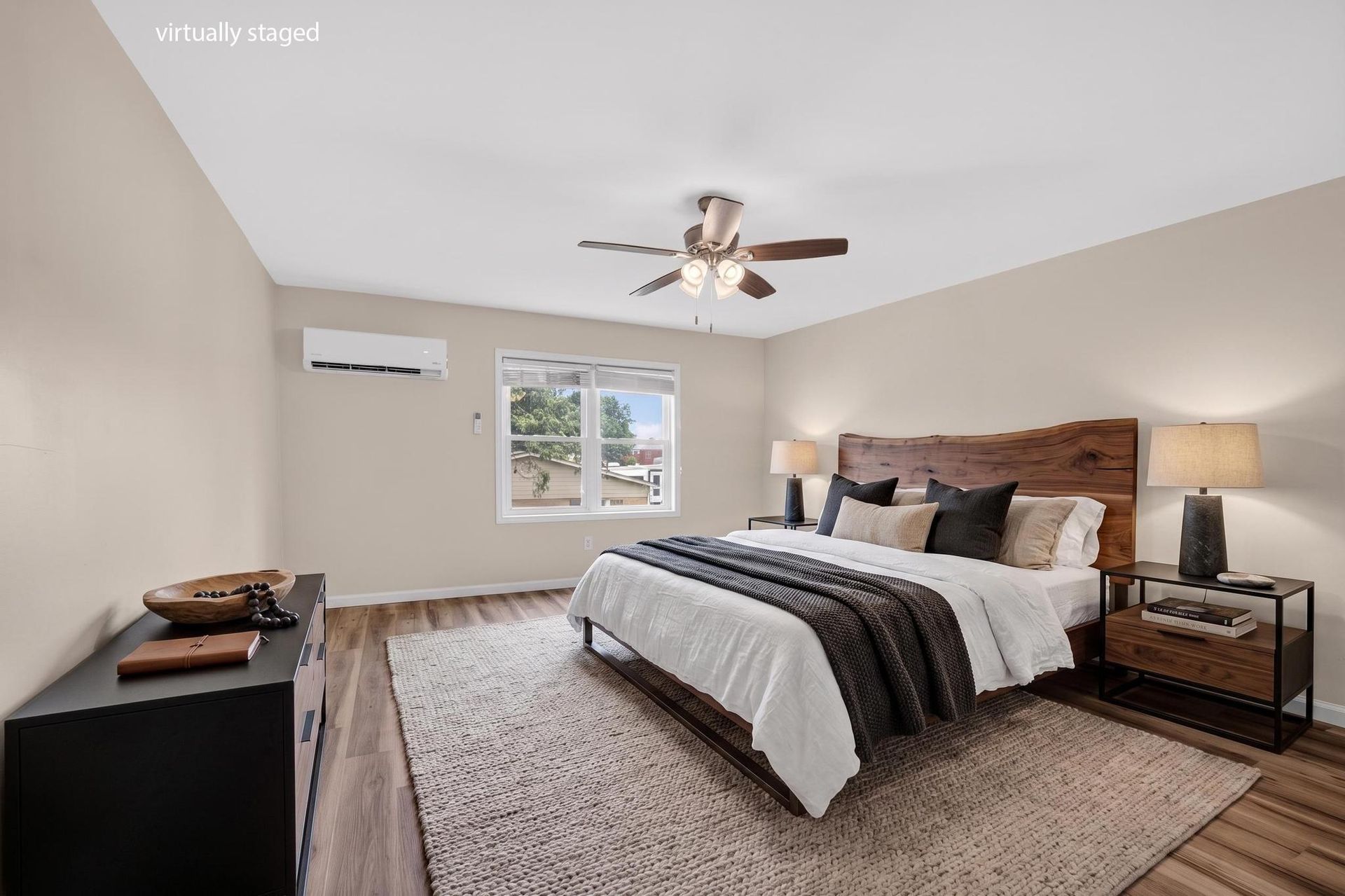 Bright bedroom with king bed, ceiling fan, bedside lamps, and window with wall AC unit
