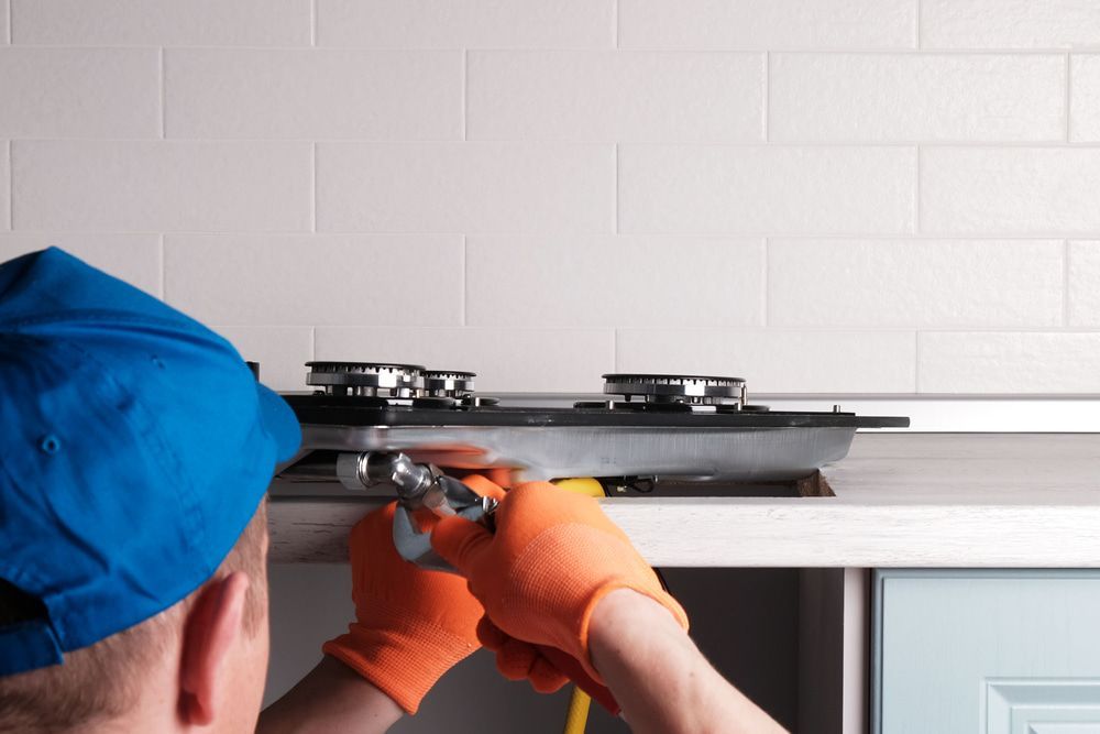 A Man Is Working On A Gas Stove In A Kitchen — Tweed Coast Appliance Repairs In Clothiers Creek, NSW