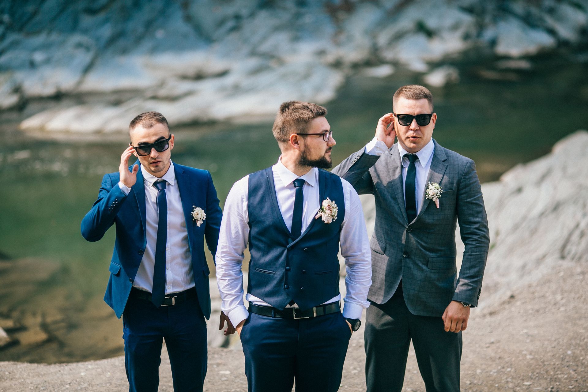 Three men in suits and sunglasses walking outdoors on a mountain path