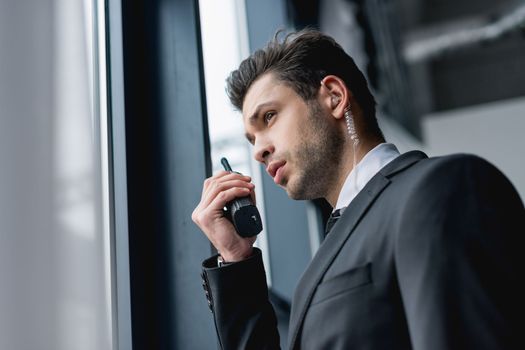 Man in a dark suit speaking into a handheld radio by a window