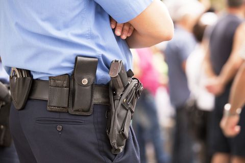 Police officer in blue uniform with holstered gun standing with arms crossed in a crowd