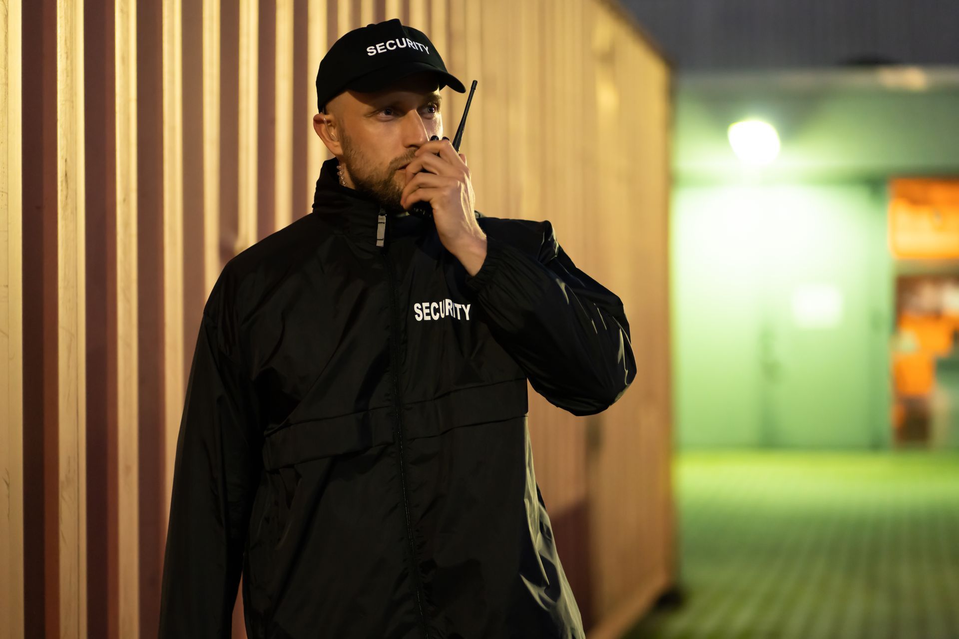 Man in black jacket and cap smoking beside a wooden wall in a dim hallway