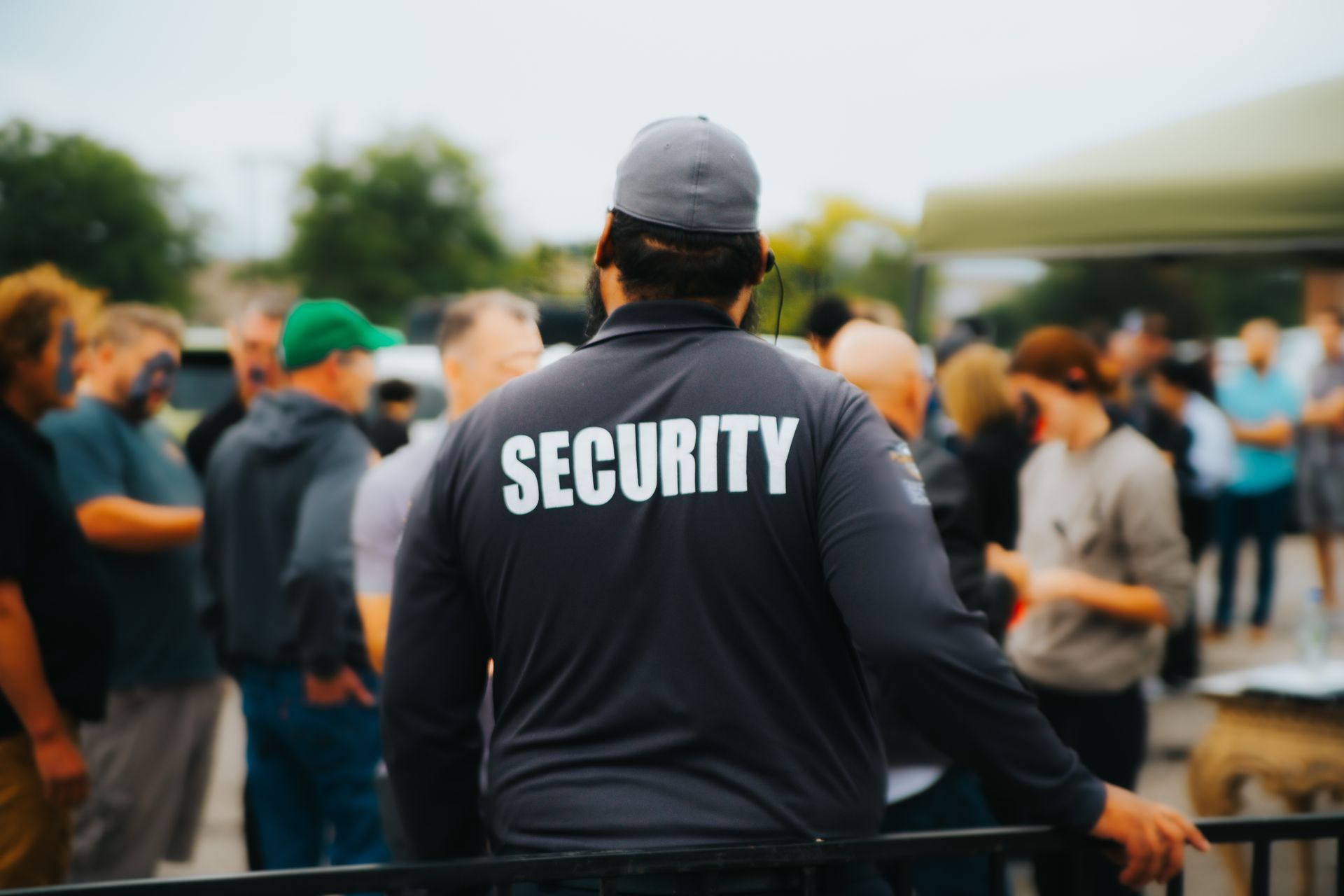 Security guard in dark jacket monitoring a crowd outdoors at an event