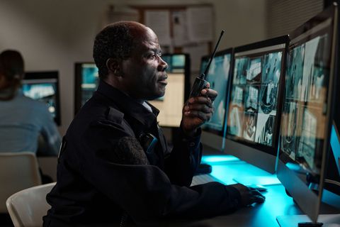 Security analyst monitoring surveillance feeds on multiple desktop screens in a dimly lit control room