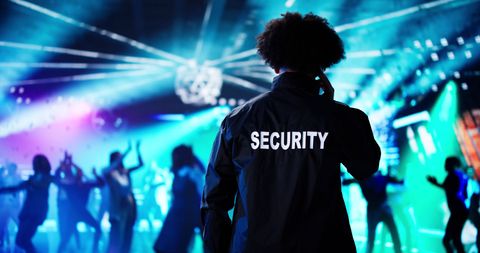 Security guard overseeing a crowded nightclub dance floor under blue and purple lights