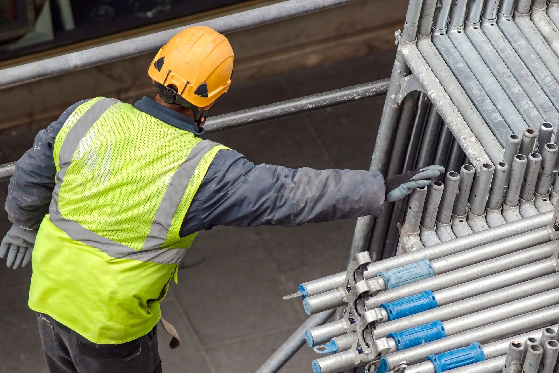 Worker in a yellow hard hat and safety vest handling metal pipes at a construction site