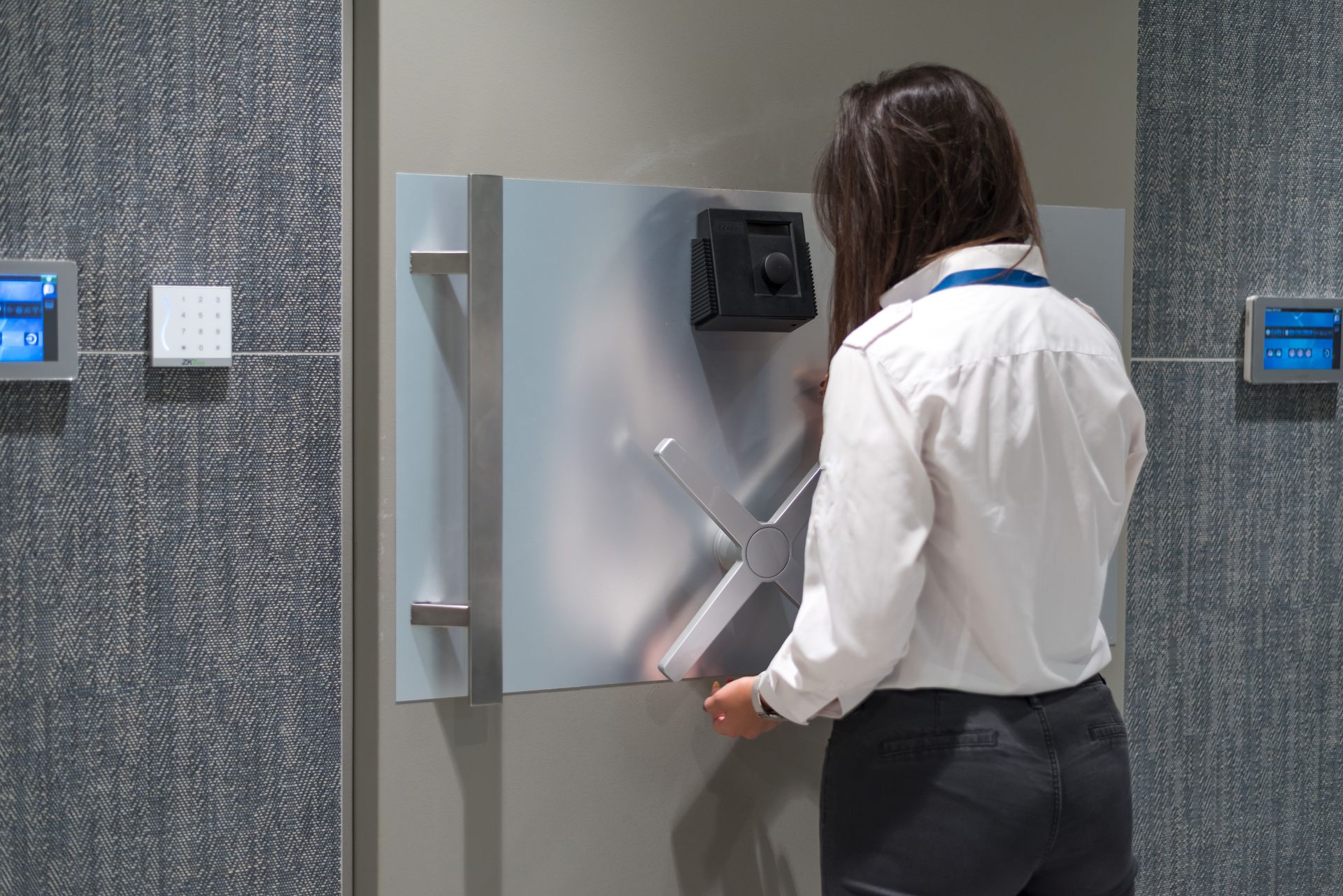Person opening a silver wall-mounted dispenser in a modern office hallway