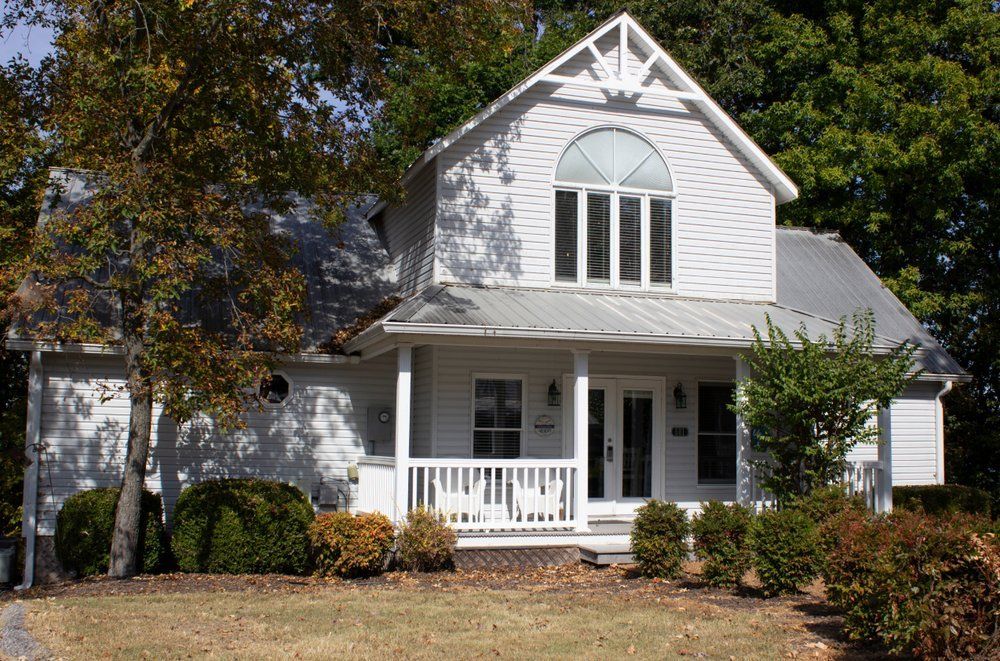 A white house with a porch and trees in the background