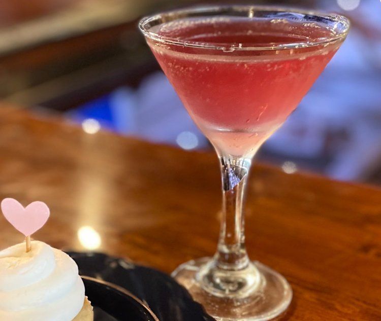 a martini glass with a pink heart on it next to a cupcake