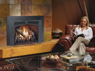 A woman is sitting in front of a fireplace reading a book.